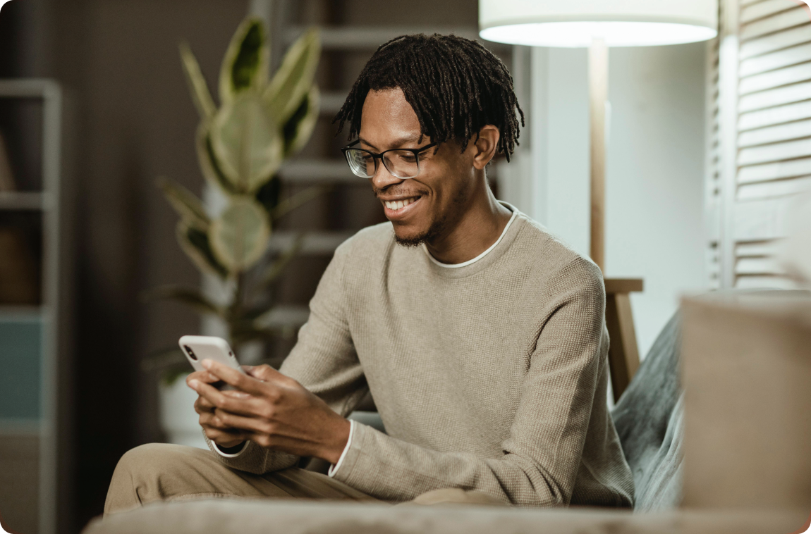 Homem negro com moletom bege sorrindo usando o celular.